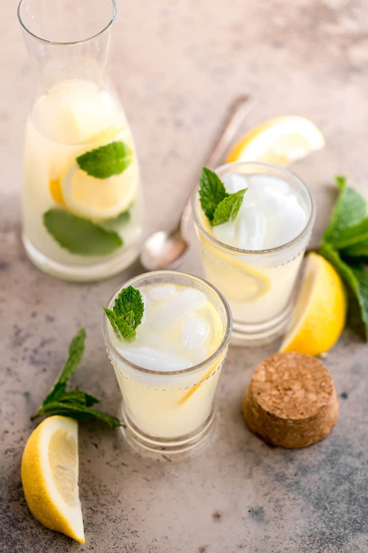 Two glasses and a pitcher of lemonade, garnished with mint and lemon slices.