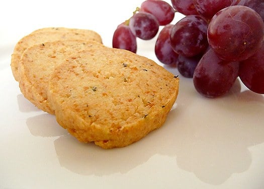 Close up image of Parmesan and thyme crackers on a white plate with grapes.