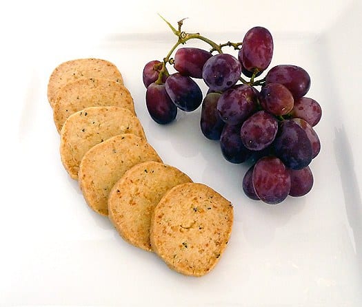 Parmesan and thyme crackers on a plate with grapes.