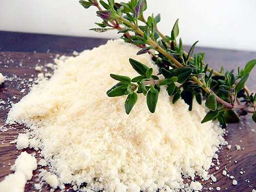 Grated Parmesan cheese and a sprig of thyme on a wood cutting board.