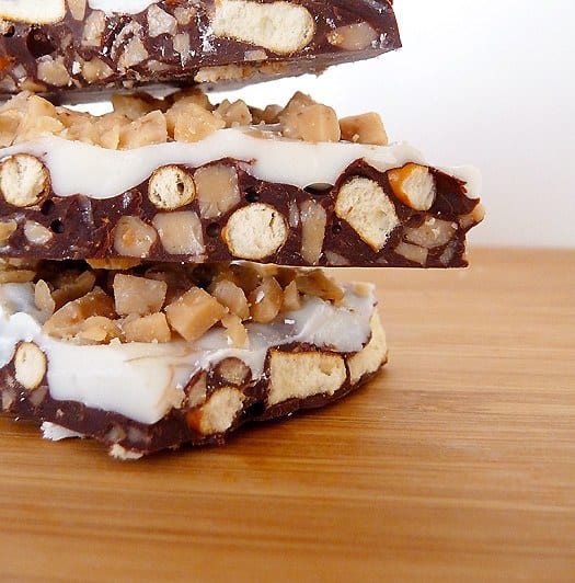 Stack of 3 pieces of toffee pretzel bark on a wood serving board.