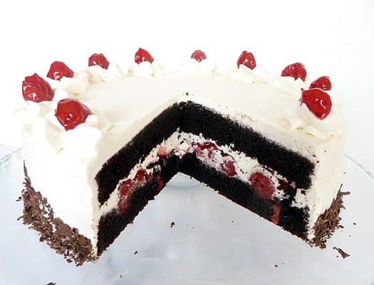 Black forest layer cake topped with frosting and cherries with a slice removed showing the inside.
