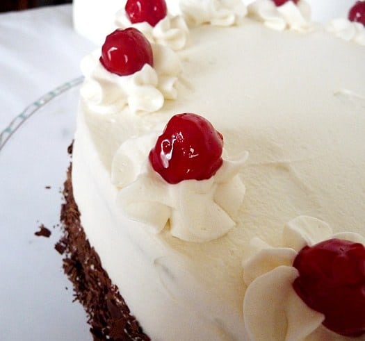 Overhead image of black forest cake topped with frosting, whipped cream dollops, and cherries.