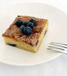 Square of blueberry butter cake topped with blueberries on a white plate with a fork.