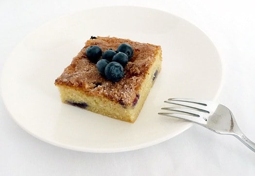 Square of blueberry butter cake topped with blueberries on a white plate with a fork.