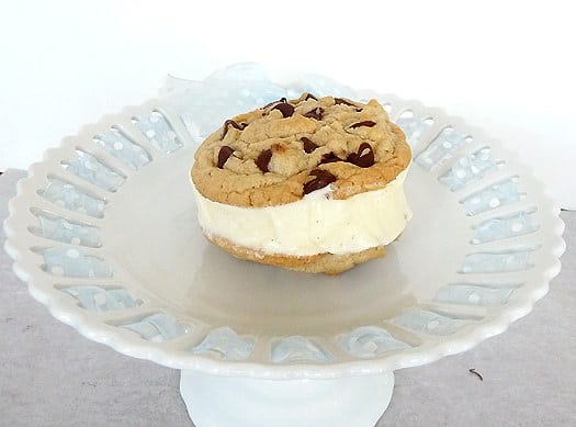 Chocolate chip cookie ice cream sandwich with vanilla ice cream on a white dessert stand.
