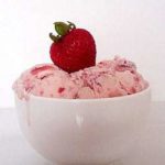 Scoops of strawberry ice cream in a white bowl topped with a fresh strawberry.