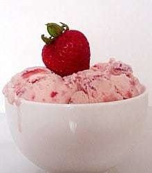 Scoops of strawberry ice cream in a white bowl topped with a fresh strawberry.
