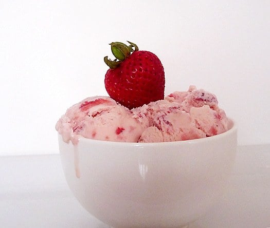 Scoops of strawberry ice cream in a white bowl topped with a fresh strawberry.