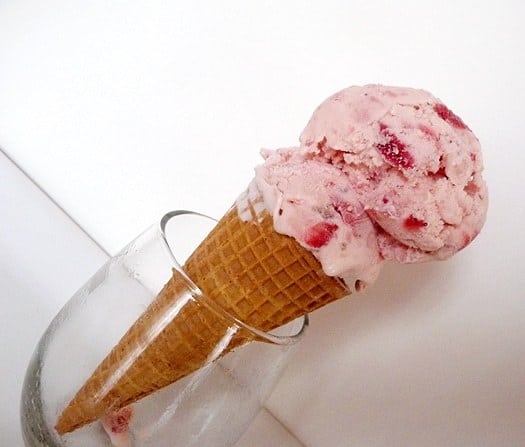 2 scoops of strawberry ice cream on a ice cream cone in a glass.