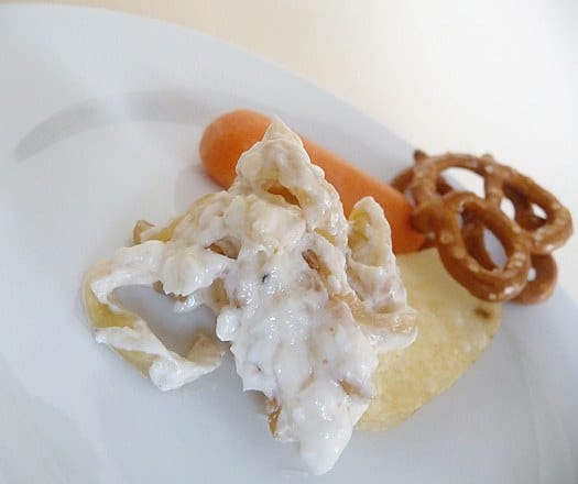 Serving of French onion dip with a carrot, pretzels, and chips on a white plate.