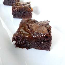 Squares of salted caramel brownies on a white plate.