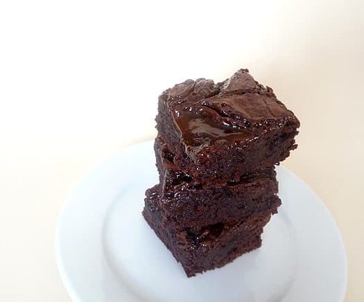 Stack of 3 salted caramel brownies on a white plate.