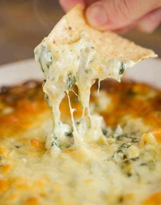 Dipping a tortilla chip into a pan of spinach artichoke dip.