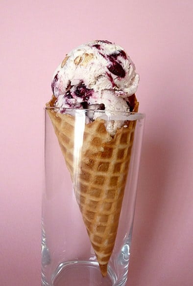 Scoops of toasted almond and candied cherry ice cream in a waffle cone in a glass.