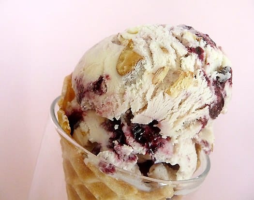 Close up image of scoops of toasted almond and candied cherry ice cream in a waffle cone.