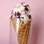 Scoops of toasted almond and candied cherry ice cream in a waffle cone in a glass.