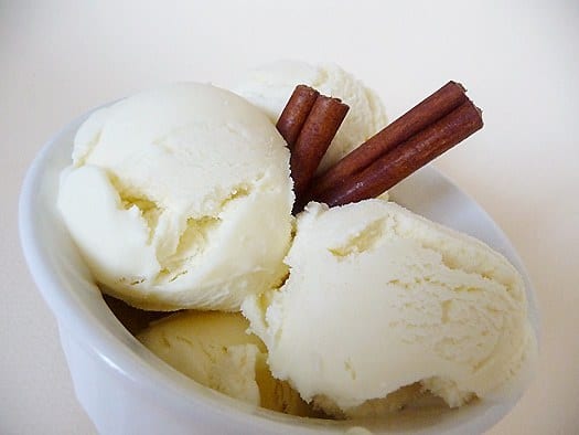 Scoops of cinnamon ice cream in a white bowl garnished with cinnamon sticks.