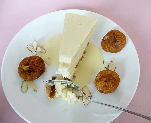 Overhead image of a forkful of fig and almond cheesecake on a white plate with a slice of cheesecake on it.