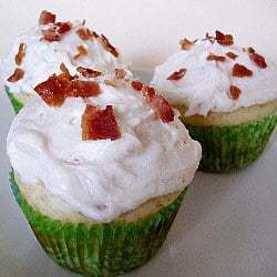 3 pancake cupcakes in green cupcake liners topped with maple frosting and sprinkled with crumbled bacon on a white plate.