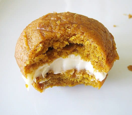 Pumpkin whoopie pie with maple cream cheese filling with a bite taken from it on a white plate.