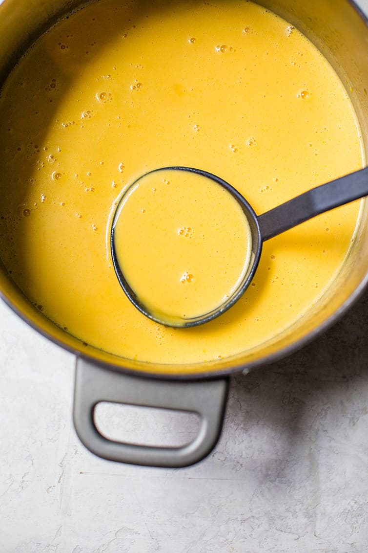 A pot of butternut squash soup with a ladle scooping some out.