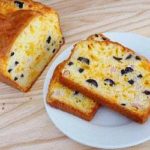 Loaf of cheese, olive, and ham bread with 2 slices of the bread on a white plate.