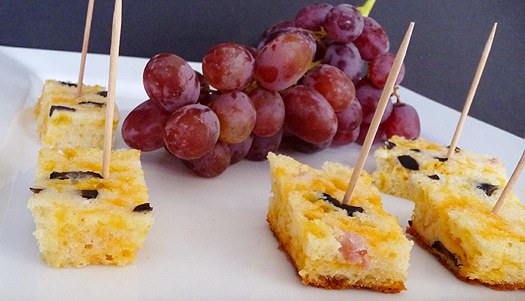 Cubes of cheese, olive, and ham bread with toothpicks for an appetizer on a white plate.