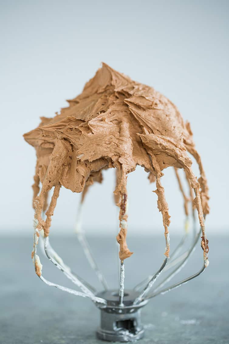 Stand mixer whisk attachment standing upright with chocolate frosting.