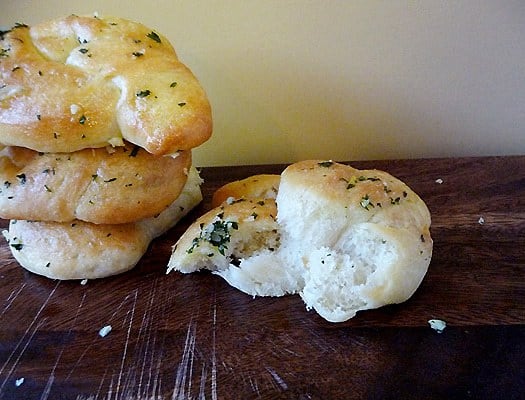 Stack of 3 garlic knots with a 4th knot on the counter with a bite taken from it.