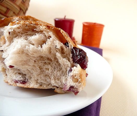 A cranberry walnut roll torn in half showing the inside texture on a white plate.
