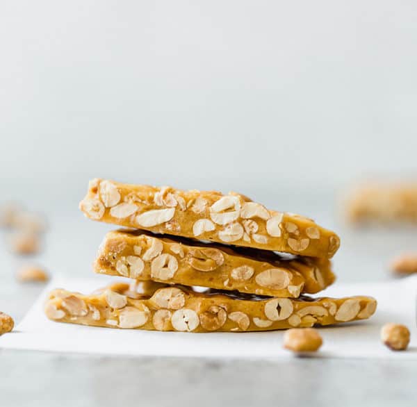Three pieces of peanut brittle stacked on a piece of parchment paper.