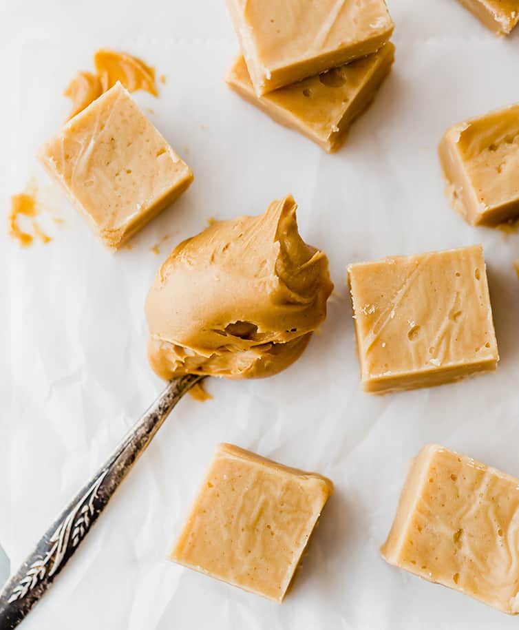 Squares of peanut butter fudge next to a spoonful of peanut butter.