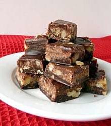 Squares of chocolate walnut fudge stacked on a white plate.