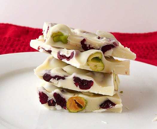 Stack of 4 pieces of pistachio and cranberry white chocolate bark on a white plate.