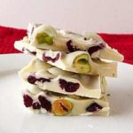 Stack of 4 pieces of pistachio and cranberry white chocolate bark on a white plate.