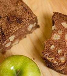 Overhead image of a loaf of apple cinnamon bread and one slice of it on a wood surface.