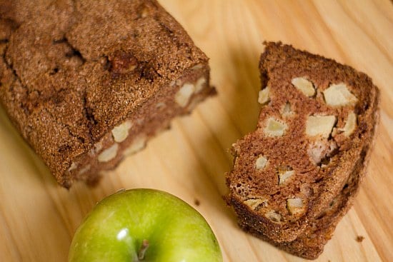 Overhead image of a loaf of apple cinnamon bread and one slice of it on a wood surface.