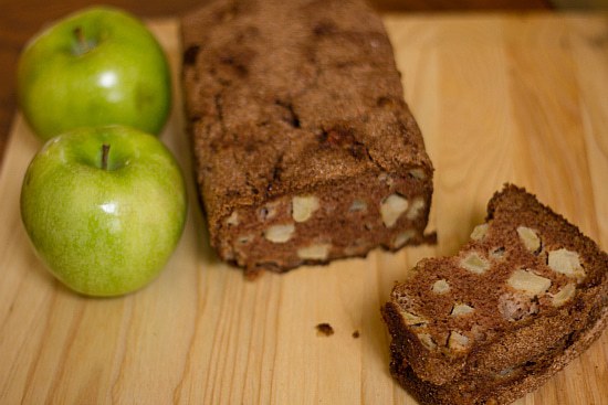 A loaf of apple cinnamon bread and one slice of it on a wood surface.