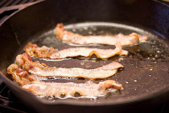 Bacon strips cooking in a skillet.