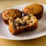 Oatmeal muffins with dates, cranberries, and pecans on a white plate with a bite taken from one muffin showing the inside texture.