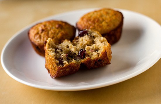 Oatmeal muffins with dates, cranberries, and pecans on a white plate with a bite taken from one muffin showing the inside texture.