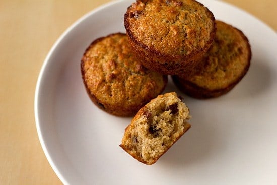 Overhead image of oatmeal muffins on a white plate with a bite taken from one showing the inside texture.