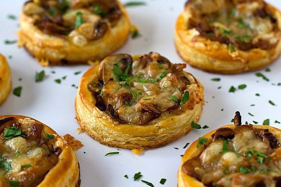 Caramelized onion, mushroom, and gruyere tartlets on a white serving plate.