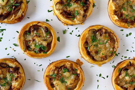 Overhead image of caramelized onion, mushroom, and gruyere tartlets on a white serving plate.