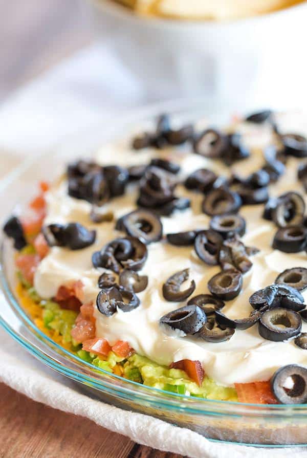 This Seven Layer Dip recipe is EASY and perfect for your Super Bowl party! Layers of refried beans, cheddar cheese, avocado, jalapeños, tomatoes, sour cream and olives! | browneyedbaker.com