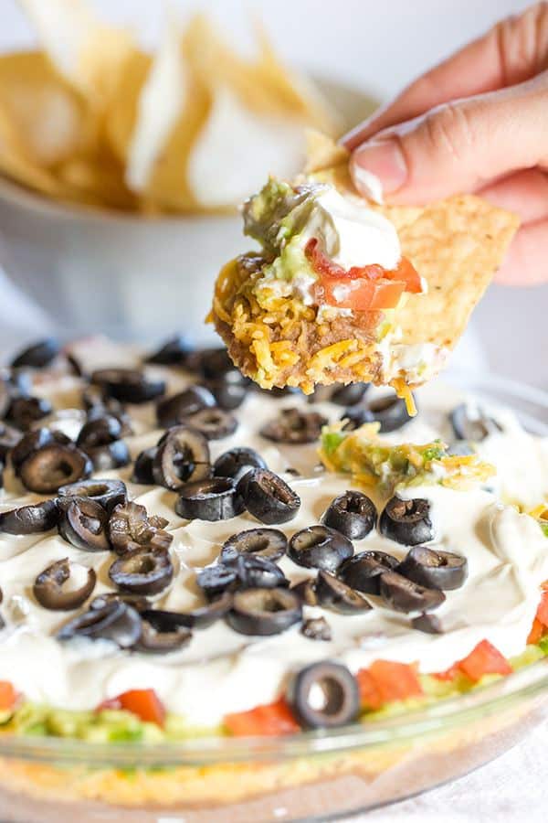 This Seven Layer Dip recipe is EASY and perfect for your Super Bowl party! Layers of refried beans, cheddar cheese, avocado, jalapeños, tomatoes, sour cream and olives! | browneyedbaker.com