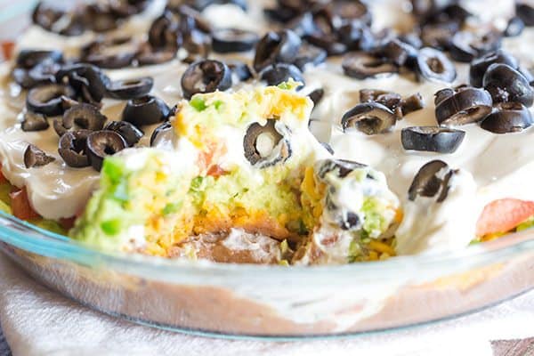 This Seven Layer Dip recipe is EASY and perfect for your Super Bowl party! Layers of refried beans, cheddar cheese, avocado, jalapeños, tomatoes, sour cream and olives! | browneyedbaker.com