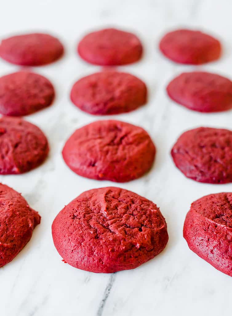 Baked red velvet whoopies on a parchment-lined baking sheet.
