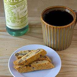 4 pieces of anisette biscotti on a white plate with a cup of coffee.